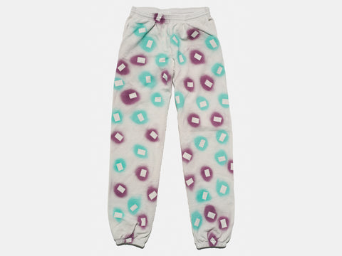 100% cotton light grey/cement sweatpants, perfectly cut, with hand-painted, purple and teal, negative cut-out squares extending across body and down legs. The pattern continues on the other side of the pants.