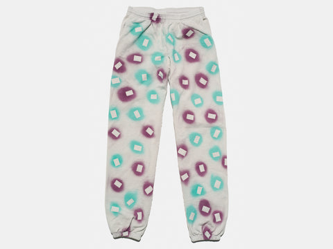 100% cotton light grey/cement sweatpants, perfectly cut, with hand-painted, purple and teal, negative cut-out squares extending across body and down legs. The pattern continues on the other side of the pants. 