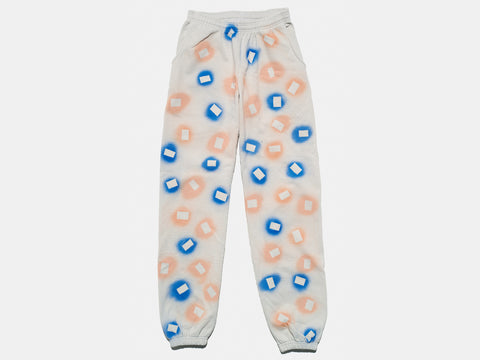 100% cotton light grey/cement sweatpants, perfectly cut, with hand-painted, blue and coral, negative cut-out squares extending across body and down legs. The pattern continues on the other side of the pants. 